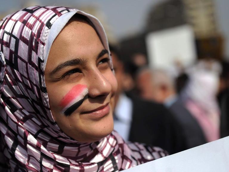 Eine junge Frau, die sich die ägyptischen Nationalfarben auf die Wange gemalt hat, steht mit einem Plakat inmitten der Demonstranten.