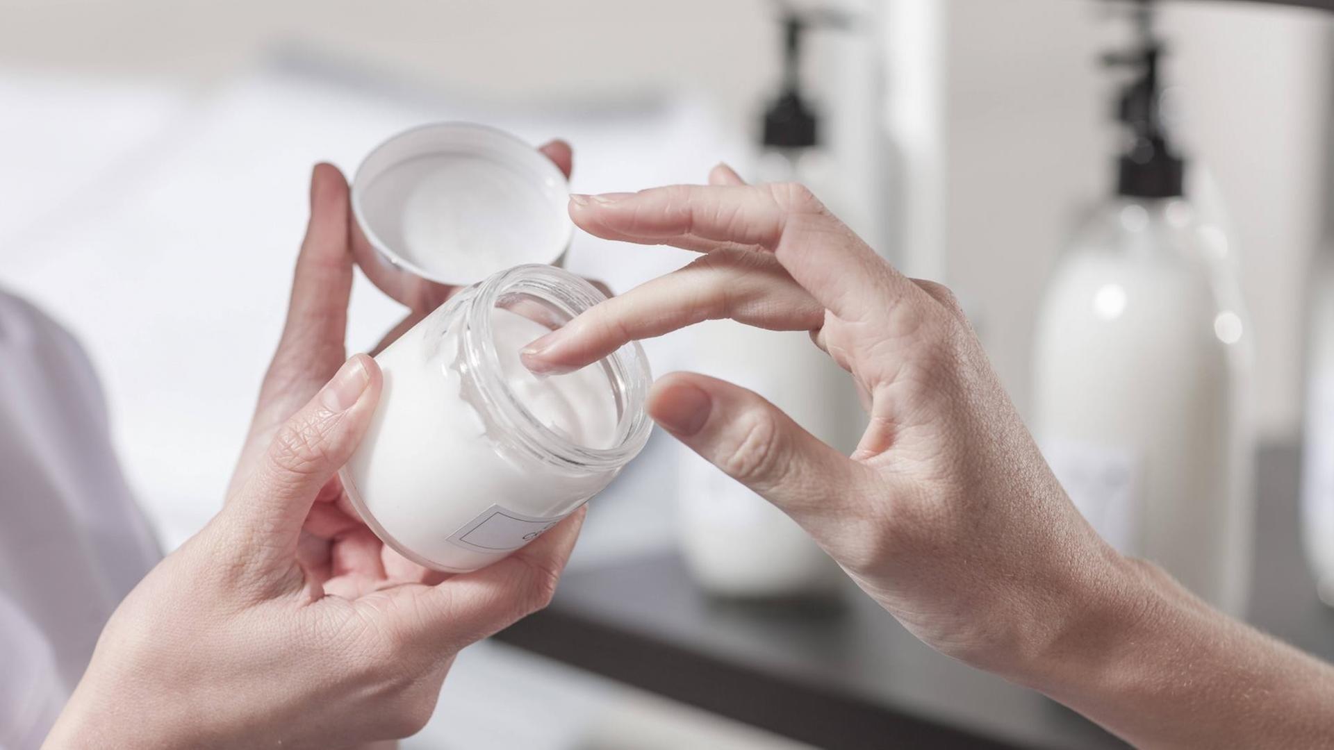 Eine Frauenhand hält einen Cremetiegel mit einer weißen Hautcreme. Eine Frauenhand hält einen Cremetiegel mit einer weißen Hautcreme.