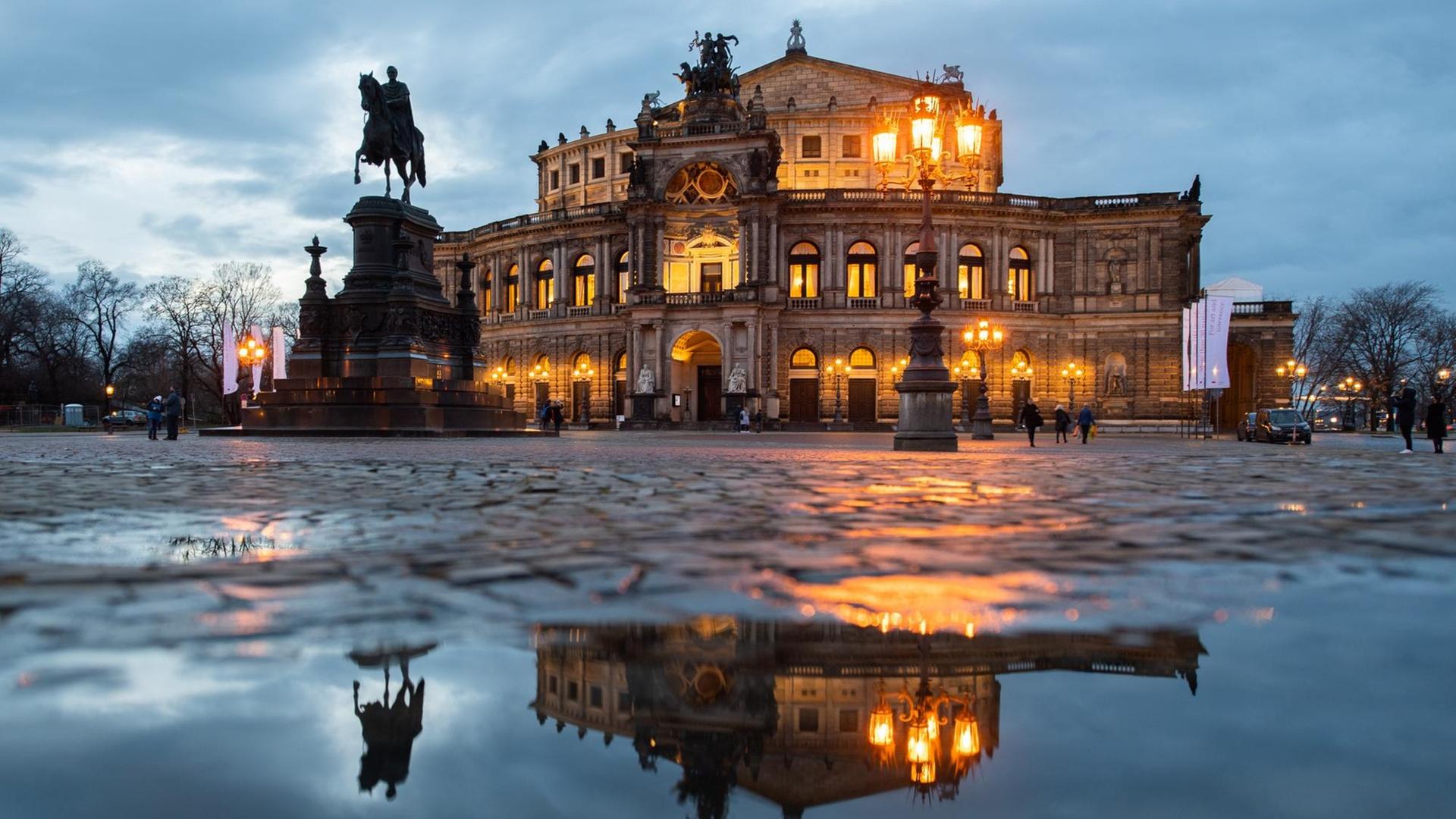 Die Semperoper und das König-Johann-Denkmal spiegeln sich am Abend in einer Pfütze auf dem Theaterplatz in Dresden. Die Semperoper und das König-Johann-Denkmal spiegeln sich am Abend in einer Pfütze auf dem Theaterplatz in Dresden.