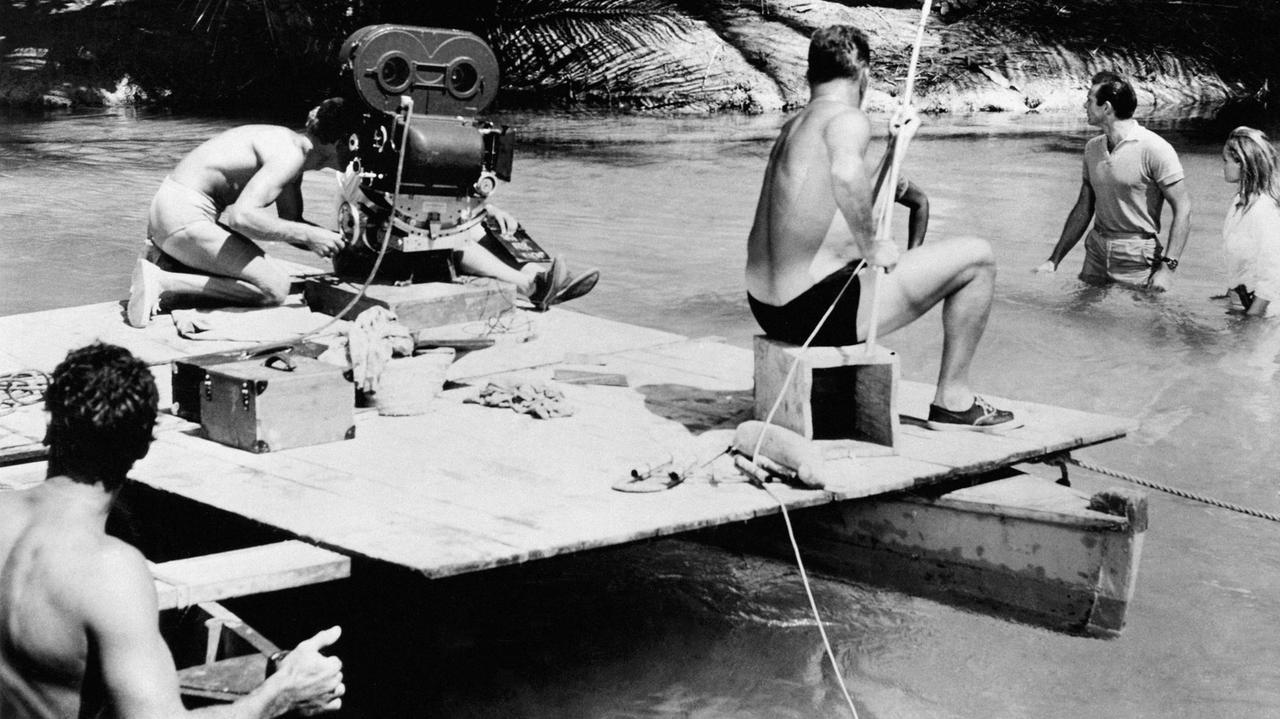 Ein Kamerateam filmt Sean Connery und Ursula Andress, die durch ein Gewässer gehen.