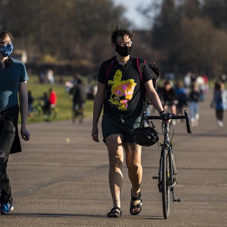 Zwei Spaziergänger mit Mundschutz, im Hintergrund mehrere Menschen bei schönem Wetter im Tempelhofer Feld Park in Berlin