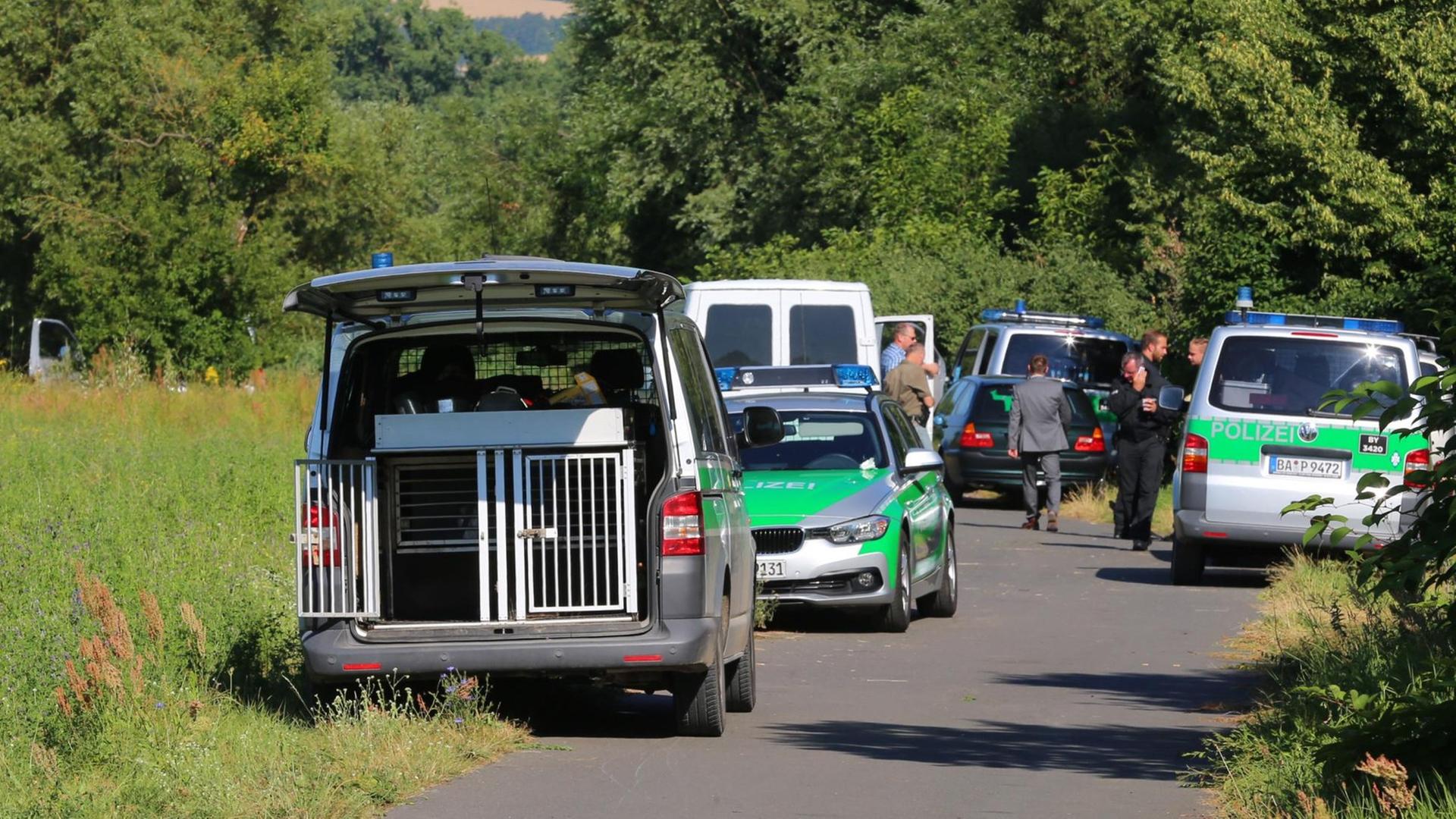 Polizisten stehen auf einem Weg bei Würzburg (Bayern) neben ihren Fahrzeugen.