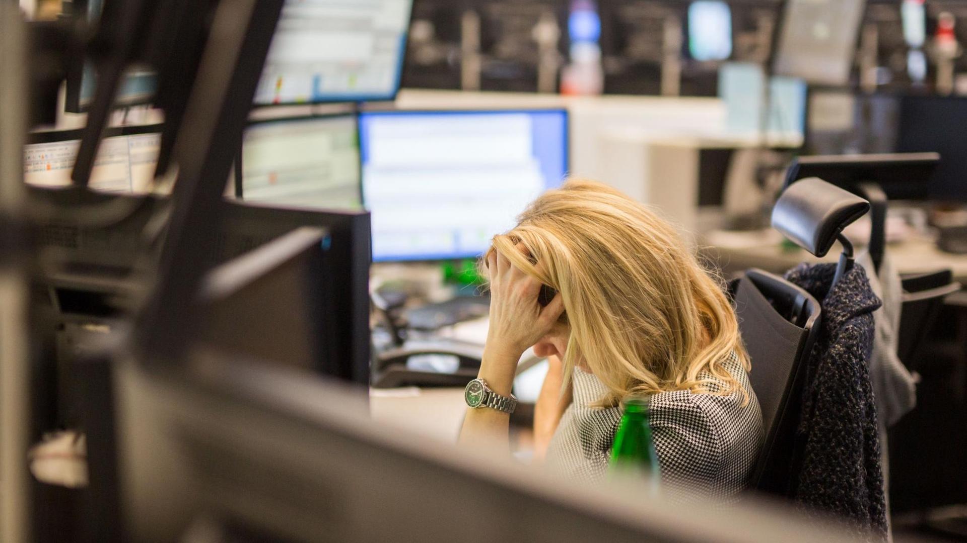 Eine Frau sitzt an ihrem Schreibtisch in der Frankfurter Börse und stützt den Kopf mit der Hand ab. Eine Frau sitzt an ihrem Schreibtisch in der Frankfurter Börse und stützt den Kopf mit der Hand ab.