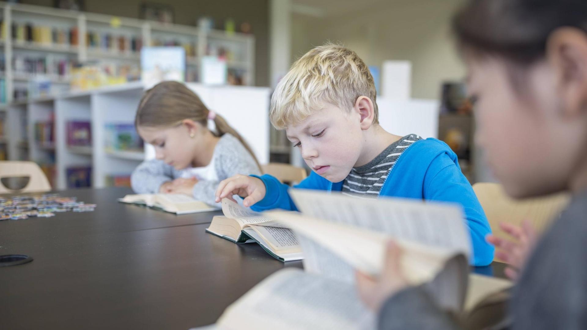 Drei Schüler sitzen in der Schulbibliothek und lesen. Sie sind tief in ihre Bücher versunken. Auf dem Tisch liegt außerdem ein Puzzle. Drei Schüler sitzen in der Schulbibliothek und lesen. Sie sind tief in ihre Bücher versunken. Auf dem Tisch liegt außerdem ein Puzzle.