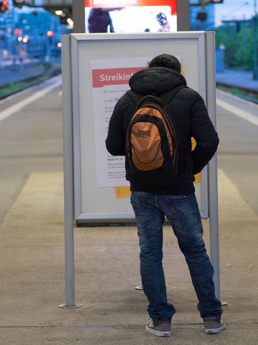 Ein Mann steht am im Bahnhof in Stuttgart an einem Bahnsteig vor einem Poster mit der Aufschrift "Streikinformation". Der Bahnsteig ist fast leer. Außer dem Mann steht ein anderer Mann auf einem Gleis.
