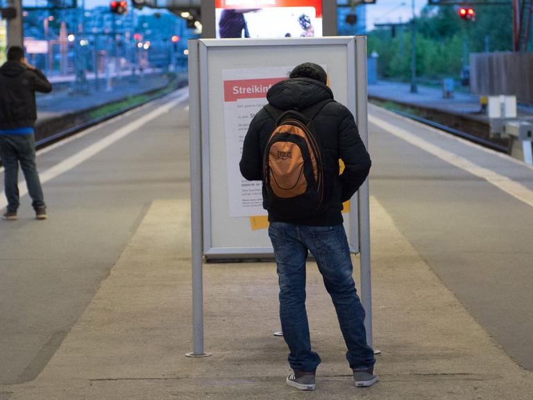 Ein Mann steht am im Bahnhof in Stuttgart an einem Bahnsteig vor einem Poster mit der Aufschrift "Streikinformation". Der Bahnsteig ist fast leer. Außer dem Mann steht ein anderer Mann auf einem Gleis.