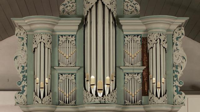 Prospekt einer sogenannten Arp-Schnitger-Orgel mit den großen Orgelpfeifen in der Mitte, eingefügt in grünes und beiges Holz, das aussen girlandenartige Verzierungen aufweist.