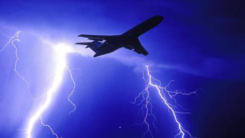 Ein Flugzeug fliegt durch eine Gewitterwolke. Im Hintergrund blitzt es.
