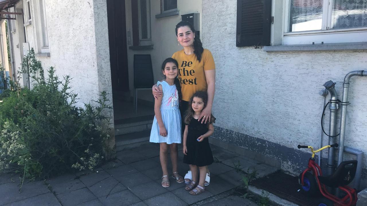 Ein junge Frau und zwei Mädchen stehen vor einer Haustür. Ein junge Frau und zwei Mädchen stehen vor einer Haustür.