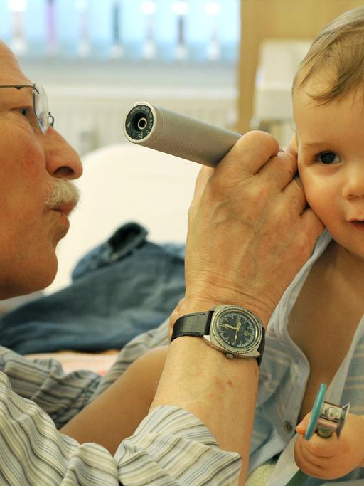 Ein Kinderarzt schaut einem Kleinkind ins Ohr.