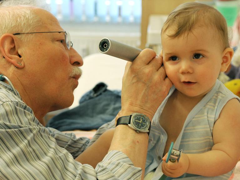 Ein Kinderarzt schaut einem Kleinkind ins Ohr.