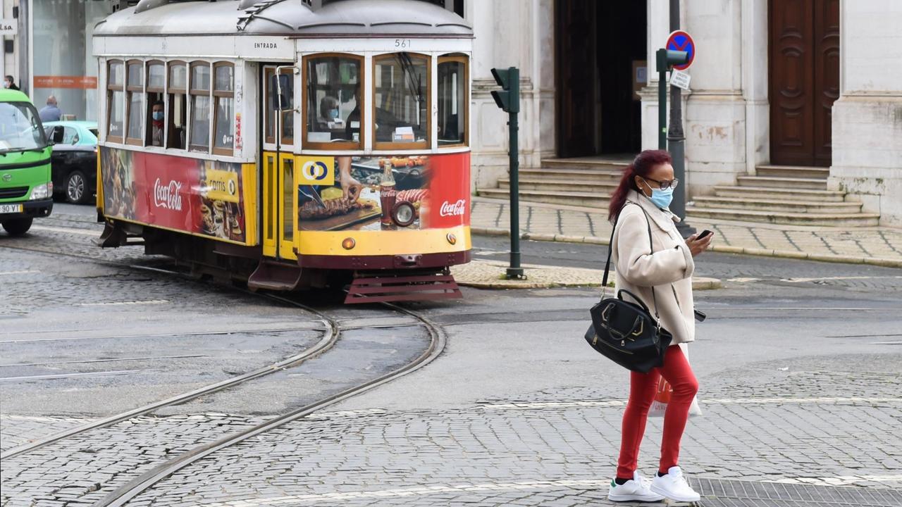 Frau mit Mund-Nasen-Bedeckung vor Straßenbahn in Lissabon. Frau mit Mund-Nasen-Bedeckung vor Straßenbahn in Lissabon.