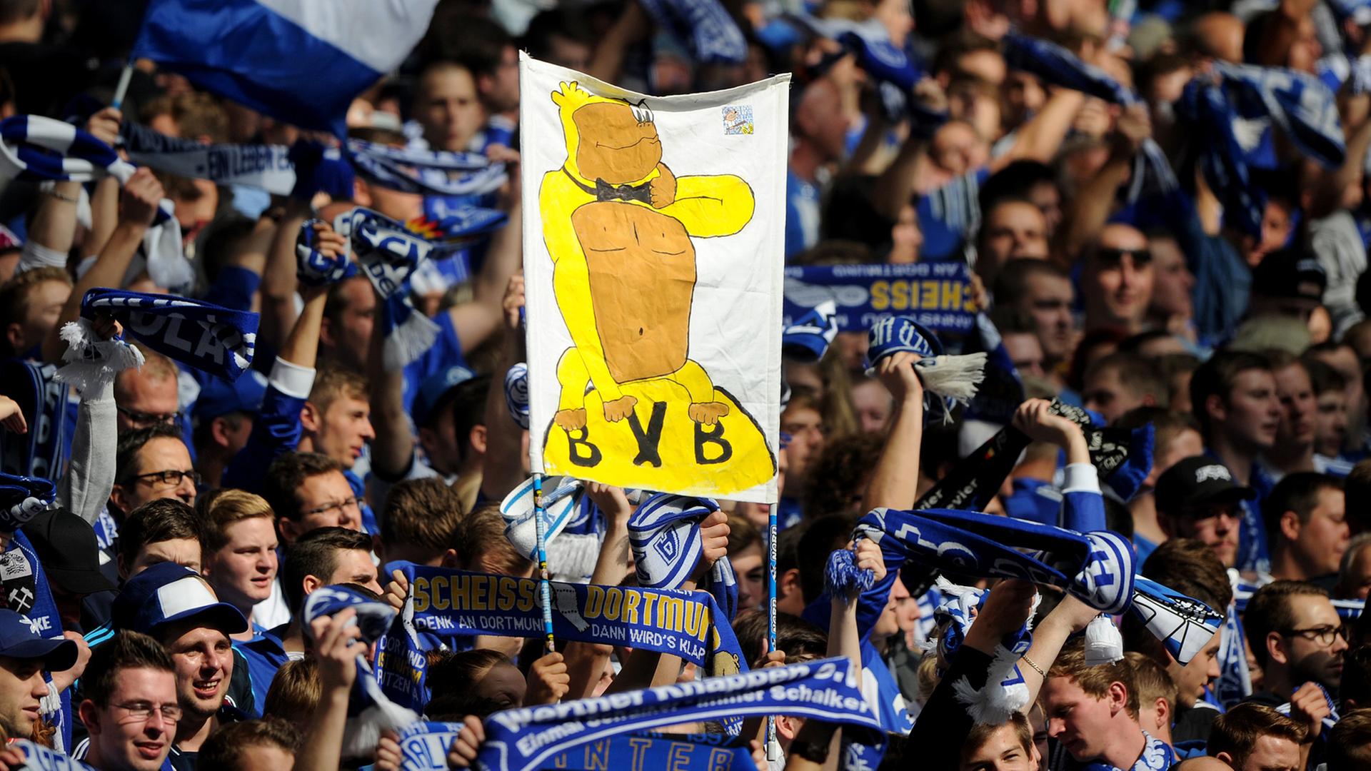 Schalke-Fans halten vor Spielbeginn ein Banner hoch, auf dem ein Affe in einem gelben Kostüm auf dem BVB-Vereinswappen sitzt. Schalke-Fans halten vor Spielbeginn ein Banner hoch, auf dem ein Affe in einem gelben Kostüm auf dem BVB-Vereinswappen sitzt.