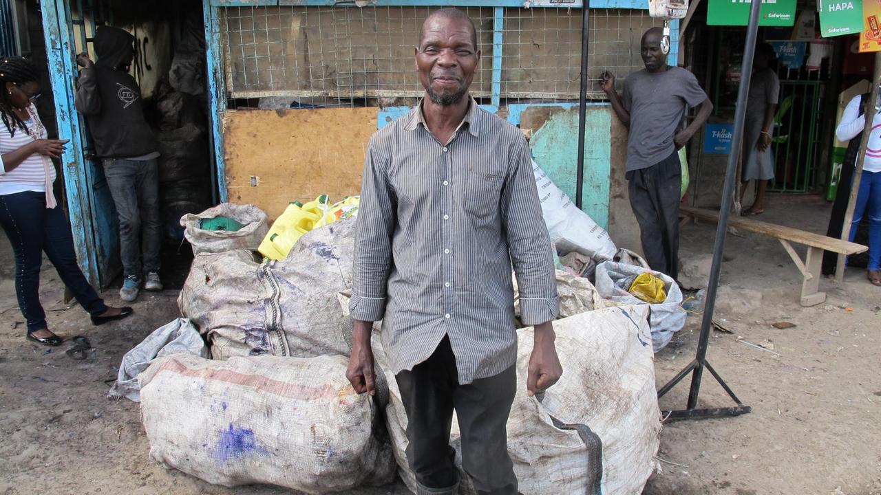 Ein Mann steht vor Müllsäcken und lächelt in die Kamera.
