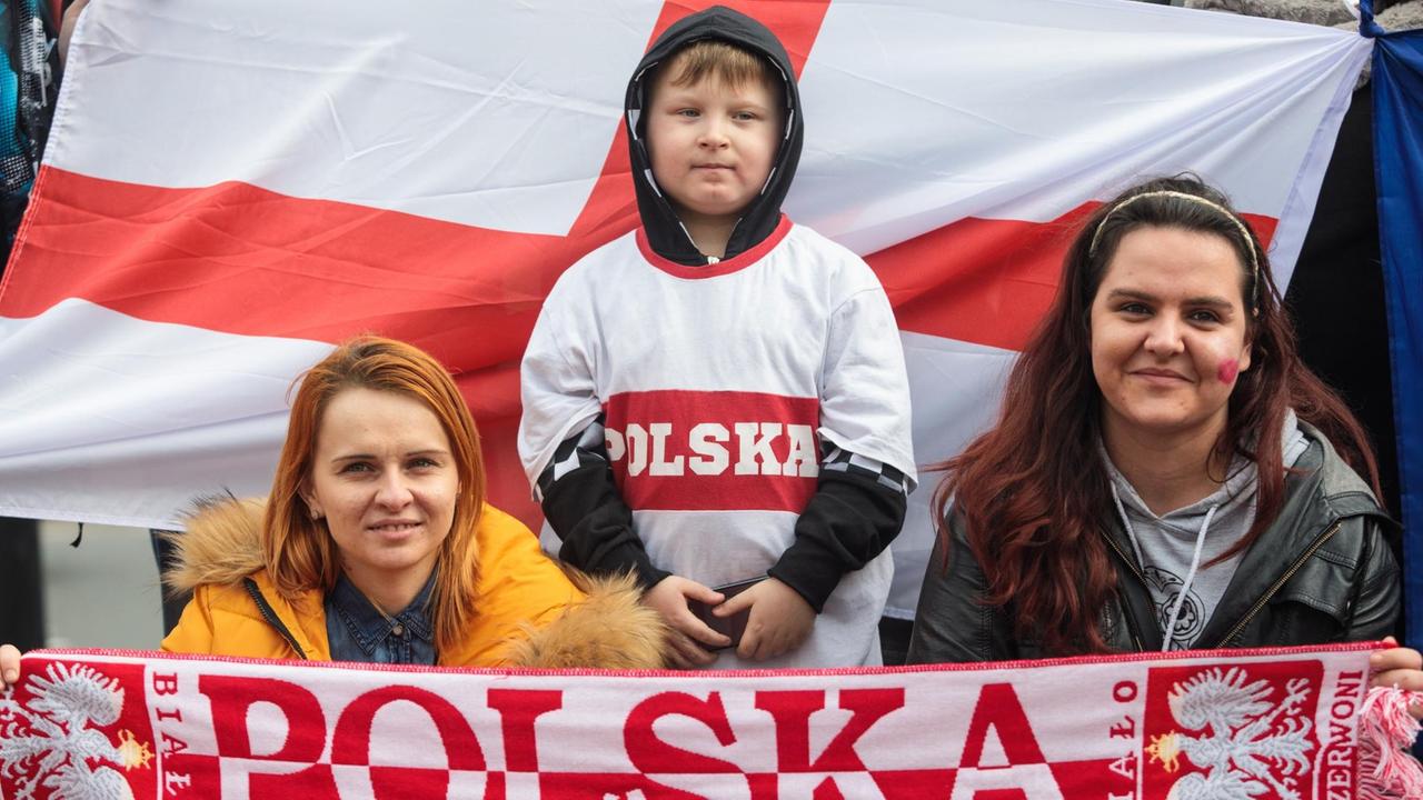 Zwei Frauen mit einem Polska-Fußballschal und ein kleiner Junge blicken in die Kamera. Hinter ihnen ist die englische Flagge zu sehen.