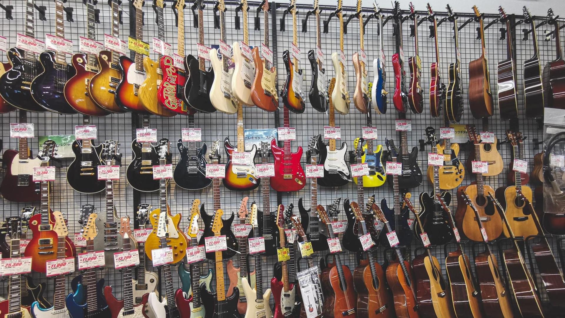 Gitarren hängen in einem Musikgeschäft in mehreren Reihen an der Wand