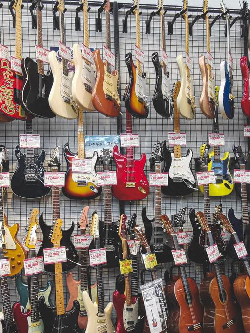 Gitarren hängen in einem Musikgeschäft in mehreren Reihen an der Wand