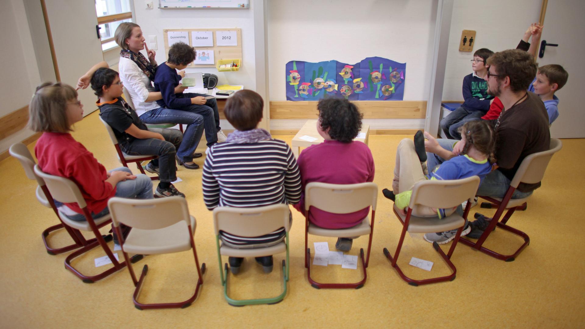 Schülerinnen und Schüler einer Inklusionsklasse in einer Förderschule sitzen im Halbkreis mit ihren Pädagogen zusammen.