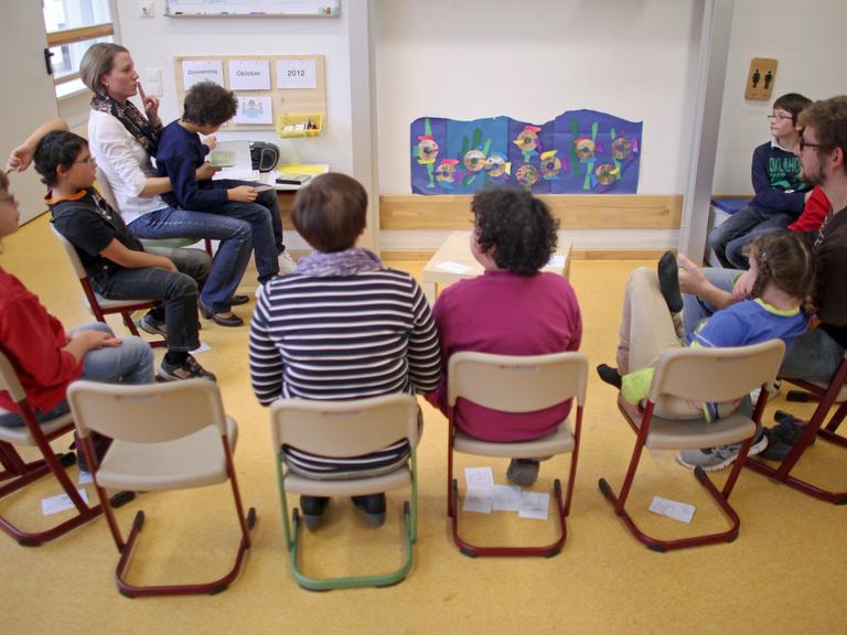Schülerinnen und Schüler einer Inklusionsklasse in einer Förderschule sitzen im Halbkreis mit ihren Pädagogen zusammen.