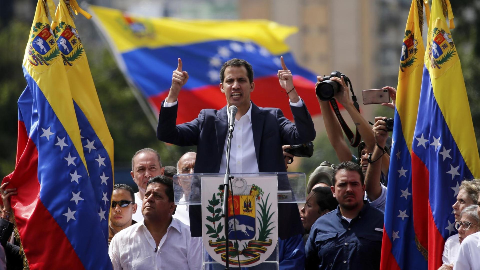 Ein Mann spricht an einem Rednerpult, um ihn herum sind Flaggen des Landes Venezuela.