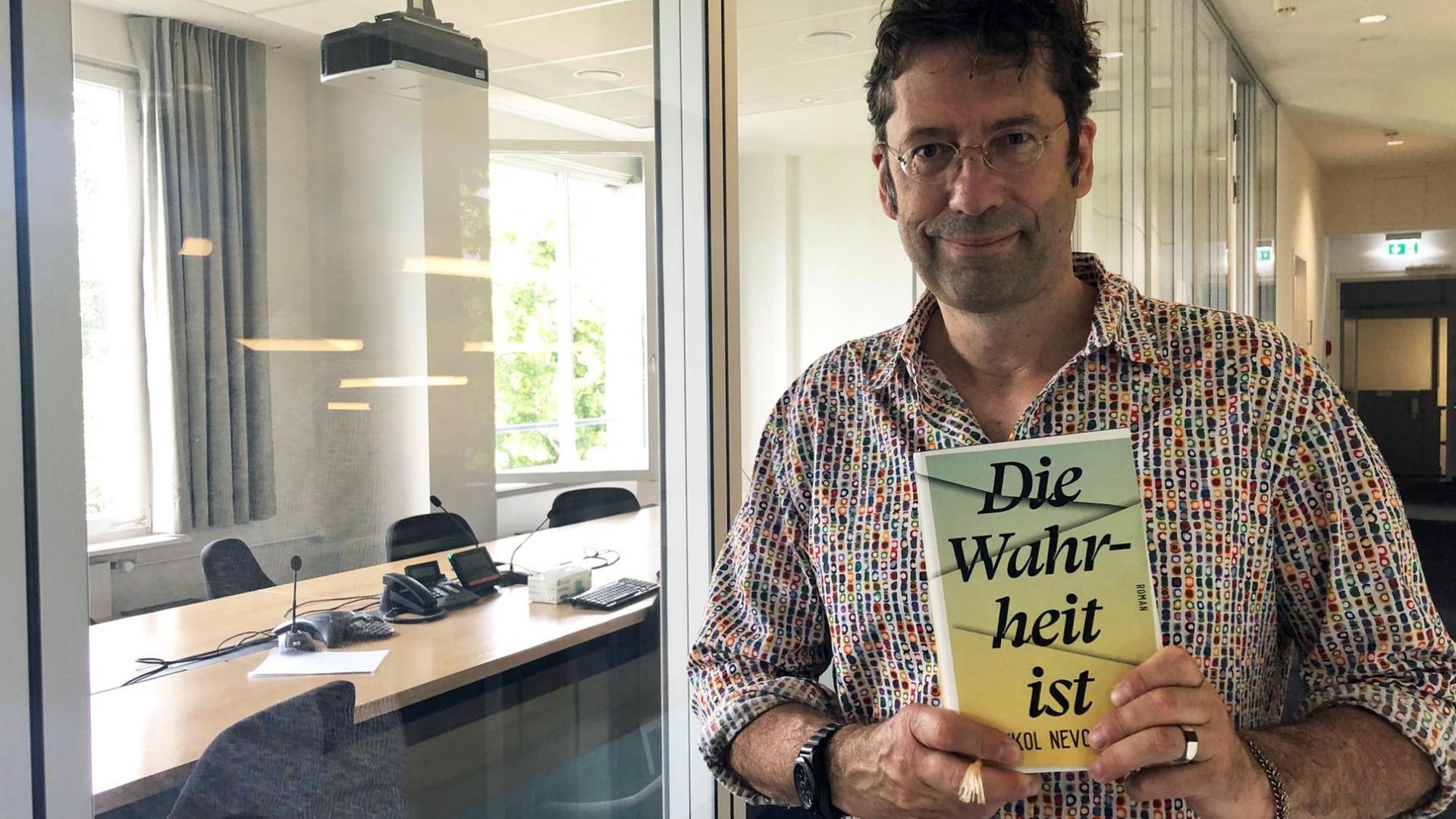 "Lesart"-Redakteur Carsten Hueck steht mit dem Buch "Die Wahrheit ist" von Eshkol Nevo im Gebäude von Deutschlandfunk Kultur.