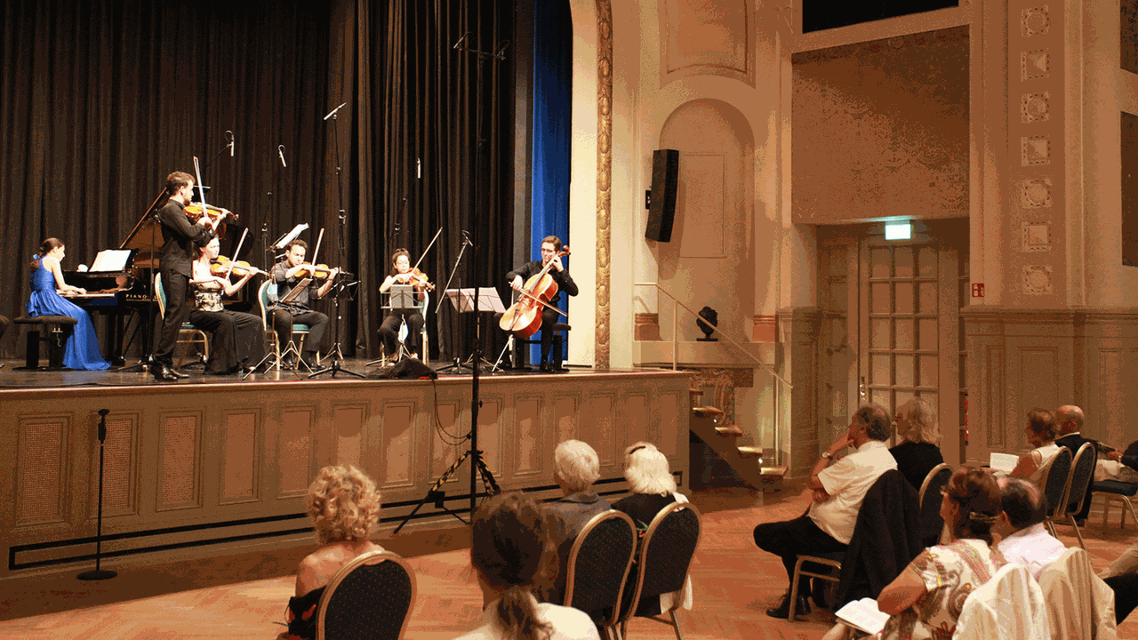 In einem historischen Theater sitzen Musiker mit Abstand vor einem locker im Saal verstreuten Publikum.