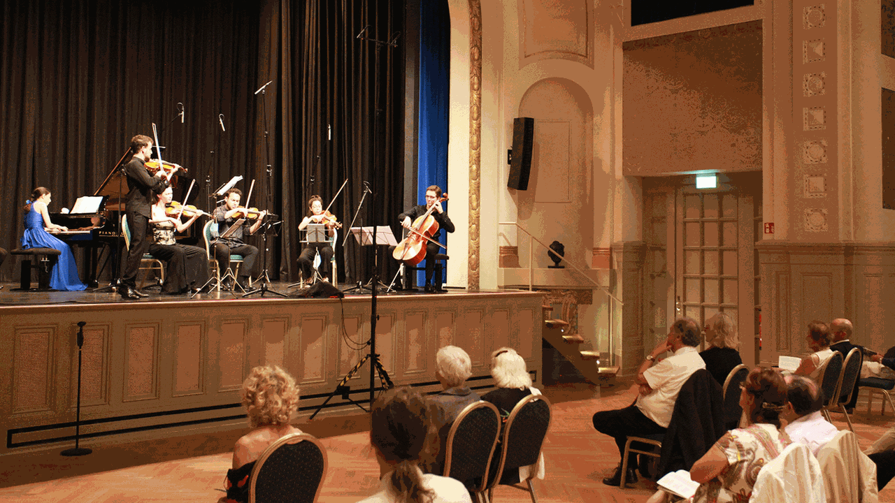 In einem historischen Theater sitzen Musiker mit Abstand vor einem locker im Saal verstreuten Publikum. In einem historischen Theater sitzen Musiker mit Abstand vor einem locker im Saal verstreuten Publikum.
