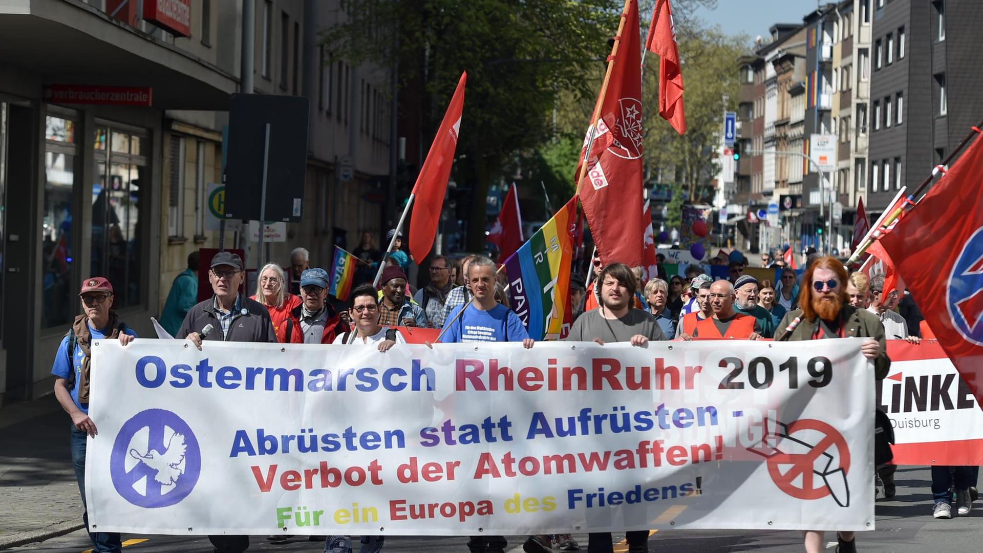Das Bild zeigt Teilnehmnde des Ostermarsches tin Duisburg. Sie halten ein Transparent hoch mit der Aufschrift: ""Abrüsten statt aufrüsten - Verbot der Atomwaffen" Das Bild zeigt Teilnehmnde des Ostermarsches tin Duisburg. Sie halten ein Transparent hoch mit der Aufschrift: ""Abrüsten statt aufrüsten - Verbot der Atomwaffen"