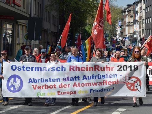 Das Bild zeigt Teilnehmnde des Ostermarsches tin Duisburg. Sie halten ein Transparent hoch mit der Aufschrift: ""Abrüsten statt aufrüsten - Verbot der Atomwaffen"
