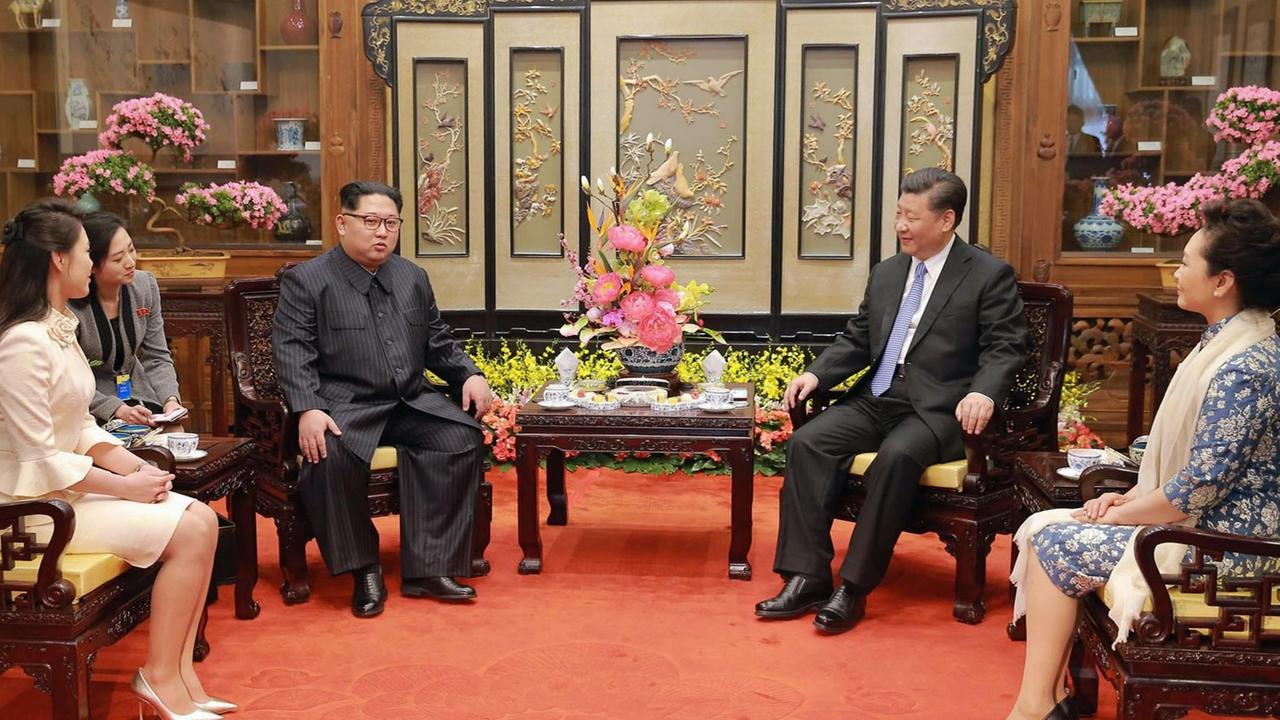 Kim Jong-Un und Xi Jinping sitzen auf Stühlen an einem Teetisch im Diaoyutai State Guesthouse in Peking. Neben ihnen haben ihre Ehefrauen Ri Sol Ju und Peng Liyuan Olatz genommen.