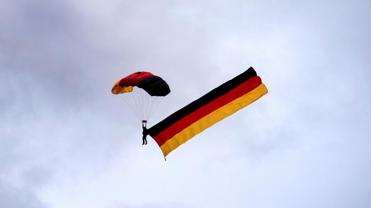 Ein Fallschirmspringer zieht am 02.10.2016 eine Deutschlandfahne am Himmel über dem Bürgerfest in Dresden (Sachsen) hinter sich her.