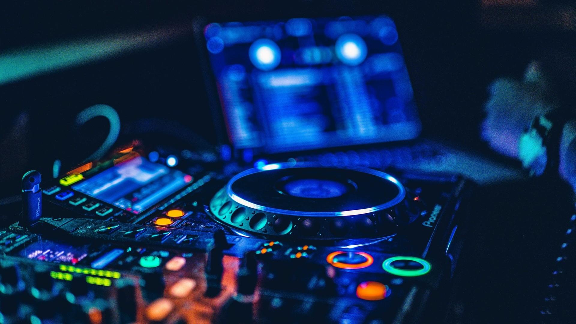 Das Bild zeigt ein leuchtendes DJ-Pult in der Dunkelheit. Das Bild zeigt ein leuchtendes DJ-Pult in der Dunkelheit.