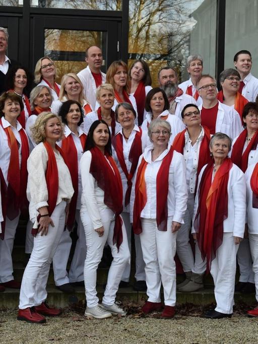 Gruppenbild des Chores vor einem Gebäude. Alle Sängerinnen und Sänger tragen weiße Kleidung und ein rotes T-Shirt.