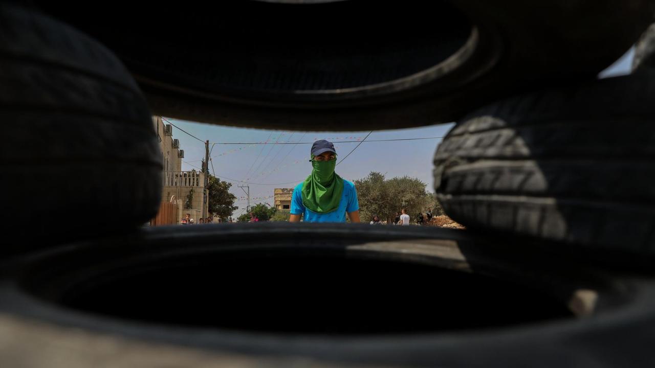 Ein palästinensicher Junge schaut - während gewaltätigen Auseinandersetzungen mit israelischen Soldaten am 31. August 2018 in Kafr Qaddum (Westbank) - durch Zwischenräume von Autoreifen, die zu einer Straßensperre gestapelt wurden.