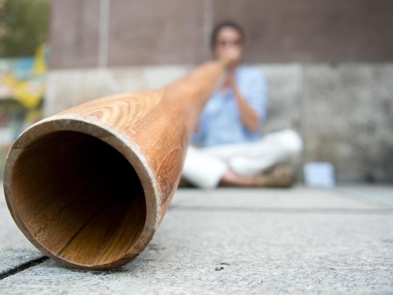 Ein Straßenmusiker spielt ein Didgeridoo, der Musiker selbst ist nur verschwommen im Hintergrund zu erkennen