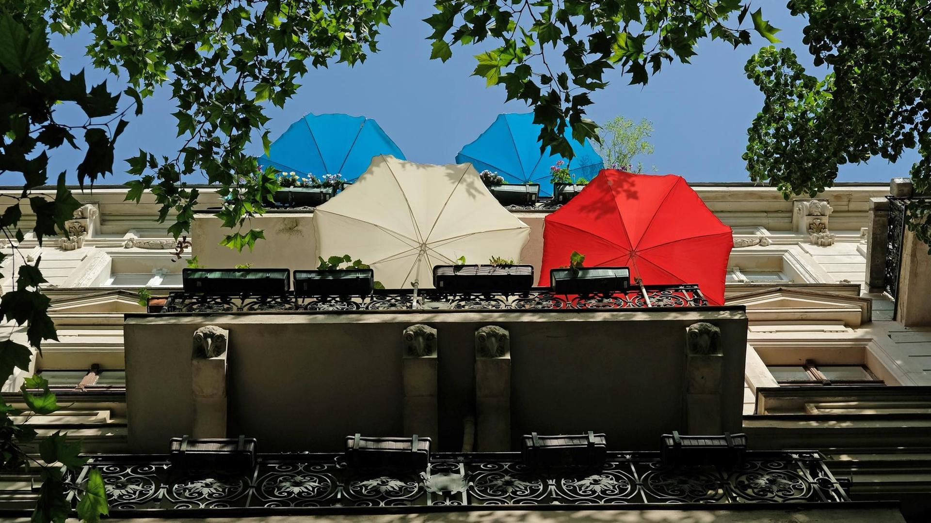 Regenschirme stehen auf Balkonen eines Wohnhauses an einem sonnigen Tag in Berlin.