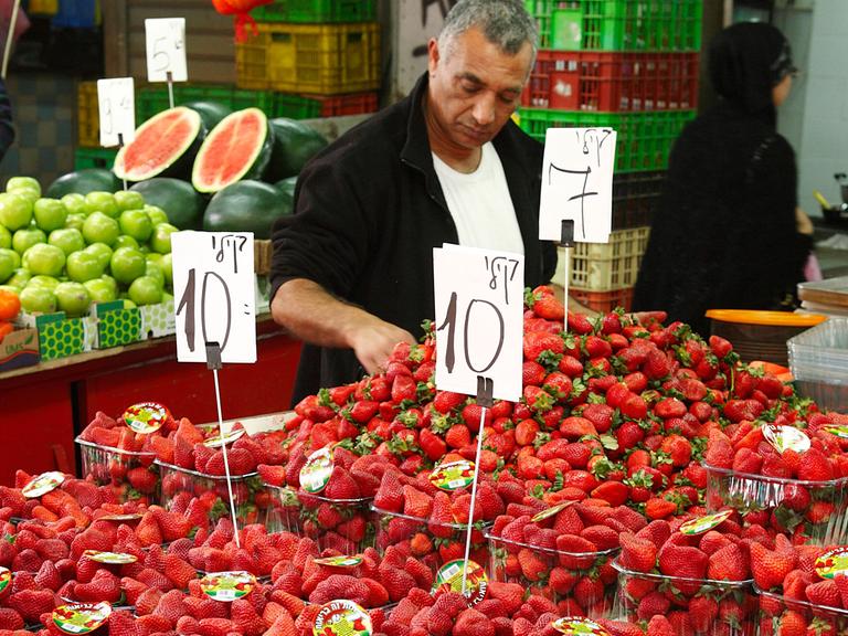 Obsthändler verkauft Plastikschalen mit frischen Erdbeeren im Carmel Markt und Basar, Tel Aviv, Israel.