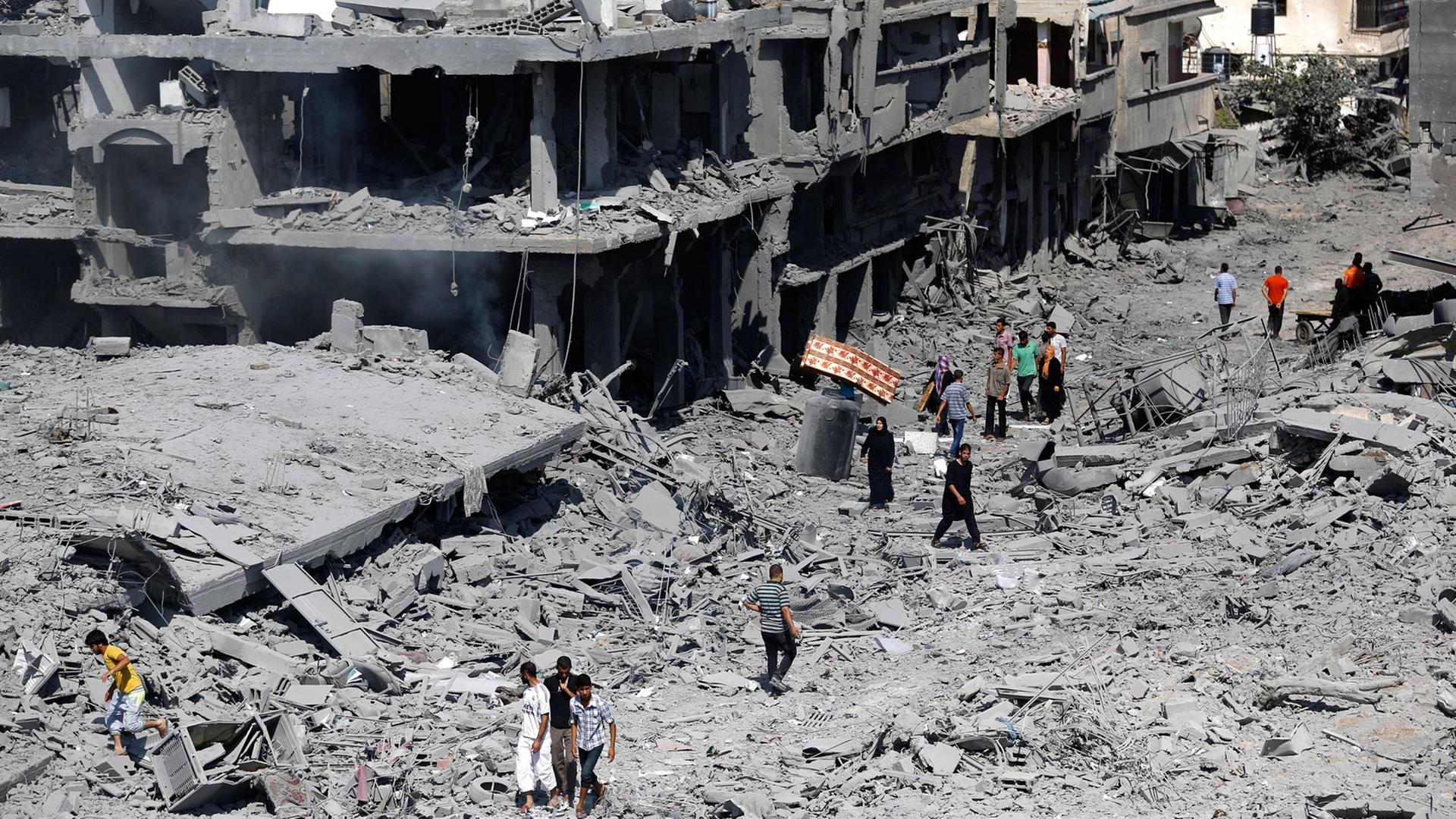 Auf dem Bild laufen Palästinenser durch eine zerstörte Straße. 