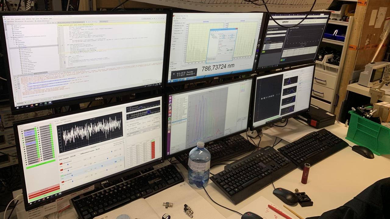 Sechs aneinander gestellte LCD-Monitore mit Zahlenkolonnen, Messkurven und grafischer Darstellung der Qubits stehen auf einem Tisch im Labor der Universität Innsbruck, davor liegen Tastaturen, Computer-Mäuse und Metallteile aus dem Experimentaufbau, vom oben hängen Kabel herunter Sechs aneinander gestellte LCD-Monitore mit Zahlenkolonnen, Messkurven und grafischer Darstellung der Qubits stehen auf einem Tisch im Labor der Universität Innsbruck, davor liegen Tastaturen, Computer-Mäuse und Metallteile aus dem Experimentaufbau, vom oben hängen Kabel herunter