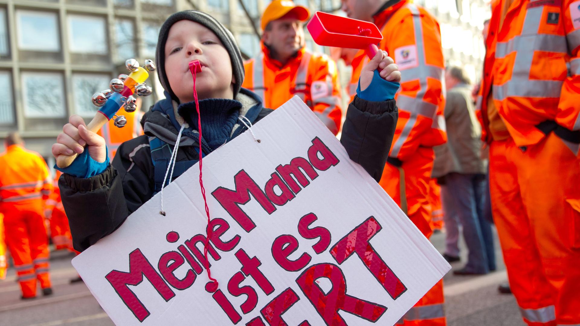 Ein Junge hält während eines Warnstreiks ein Plakat mit der Aufschrift "Meine Mama ist es Wert"
