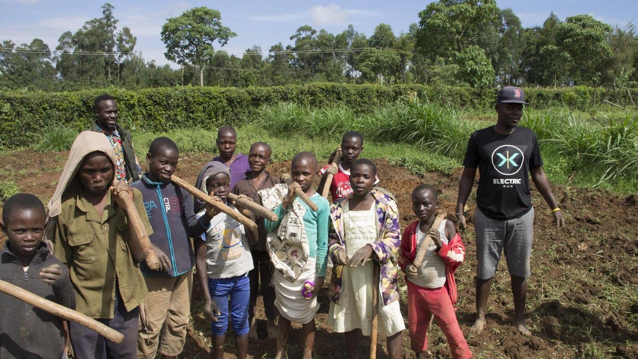 Eine Gruppe von afrikanischen Jungen und ihr Sozialarbeiter mit Gartengeräten im Gemüsegarten. Eine Gruppe von afrikanischen Jungen und ihr Sozialarbeiter mit Gartengeräten im Gemüsegarten.