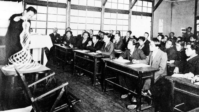 Das Bild zeigt japanische Studierende, die in einem Klassenraum eine Lehrer beobachten, der eine Vasen-Form vorführt.
