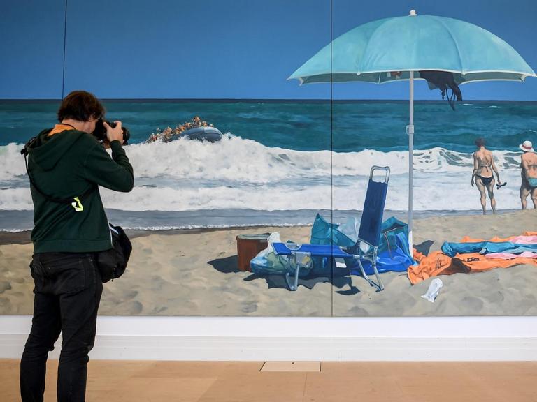 Ein junger Mann fotografiert das Gemälde "Beach of Plenty" des Künstlers Michael Kvium in der Ausstellung "Durch Mauern gehen" zum 30. Jahrestag des Falls der Berliner Mauer im Martin-Gropius-Bau. Die Ausstellung läuft vom 12.09.2019 bis 19.01.2020