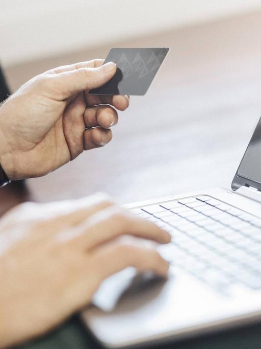 Ein Mann hält eine Kreditkarte in den Händen und zahlt online über einen Laptop.