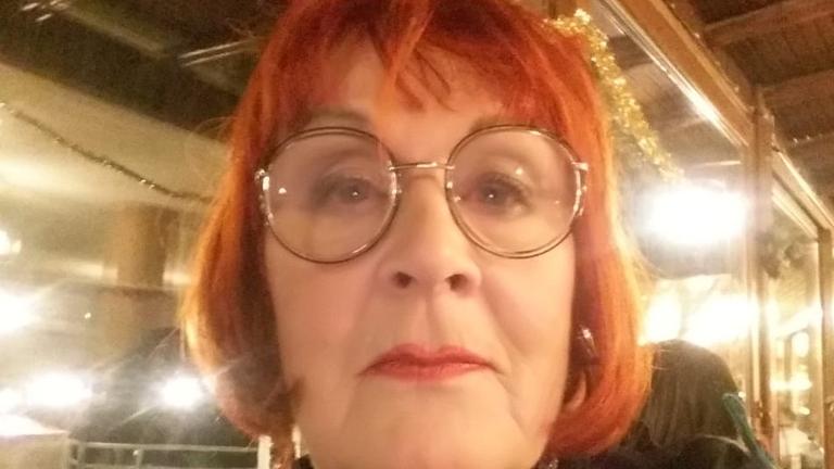 Eine rothaarige ältere Frau mit rotem Lippenstift schaut durch eine große Brille in die Kamera. Eine rothaarige ältere Frau mit rotem Lippenstift schaut durch eine große Brille in die Kamera.