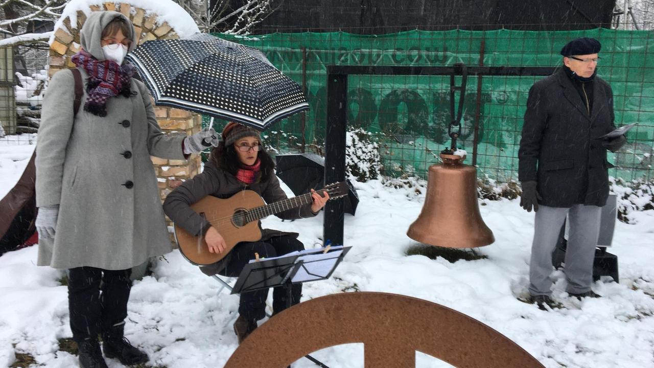 Beate Engelke, Liedermacherin Nicole Mercier und Pfarrer Matthias Engelke. Engelke hält einen Regenschirm über Mercier, die Gitarre spielt. Beate Engelke, Liedermacherin Nicole Mercier und Pfarrer Matthias Engelke. Engelke hält einen Regenschirm über Mercier, die Gitarre spielt.