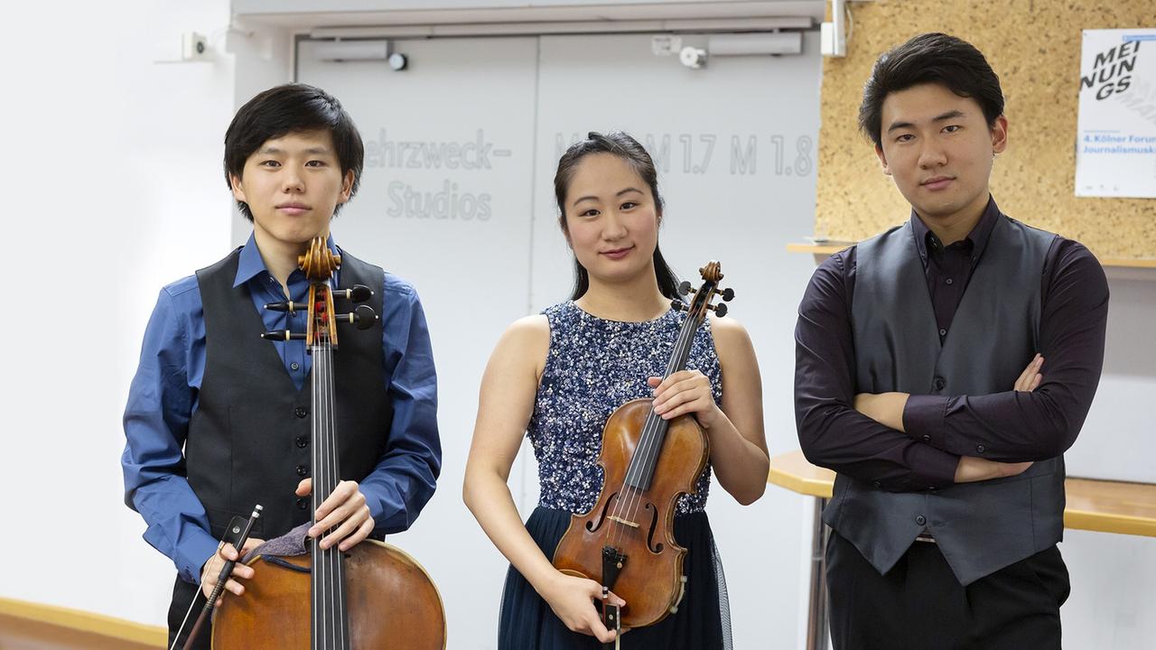 v.l.: Yu Ito (Vc), Kyoko Ogawa (Vl) und Kosuke Akimoto (Kl) posieren vor einer weißen Tür im Deutschlandfunk Köln v.l.: Yu Ito (Vc), Kyoko Ogawa (Vl) und Kosuke Akimoto (Kl) posieren vor einer weißen Tür im Deutschlandfunk Köln
