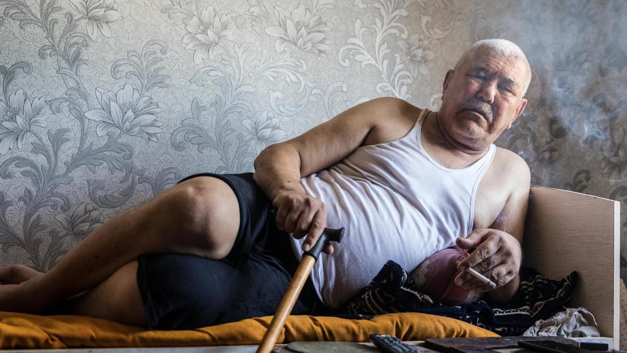 Alter Mann auf dem Bett, gestützt auf seinen Arm.