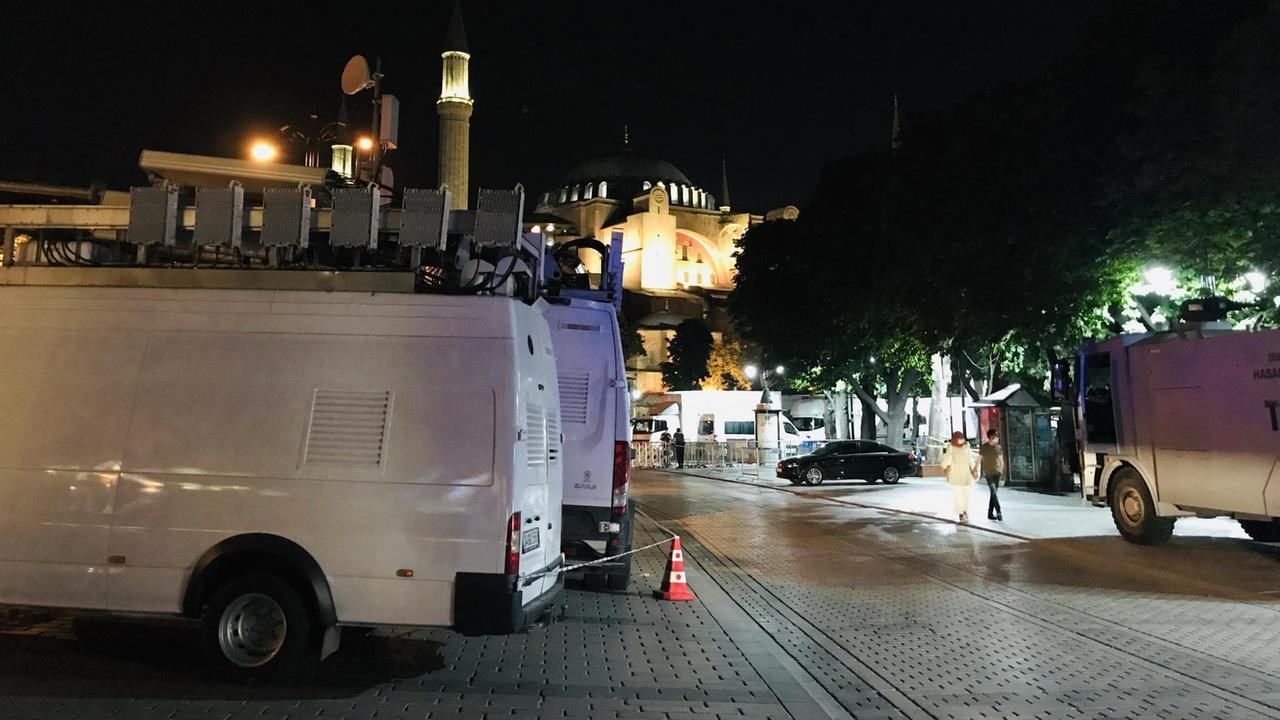 Mehrere Fernsehübertragungswagen, groß und weiß mit Satellitenschüsseln, stehen im Dunkeln vor der Hagia Sophia in Istanbul. Mehrere Fernsehübertragungswagen, groß und weiß mit Satellitenschüsseln, stehen im Dunkeln vor der Hagia Sophia in Istanbul.