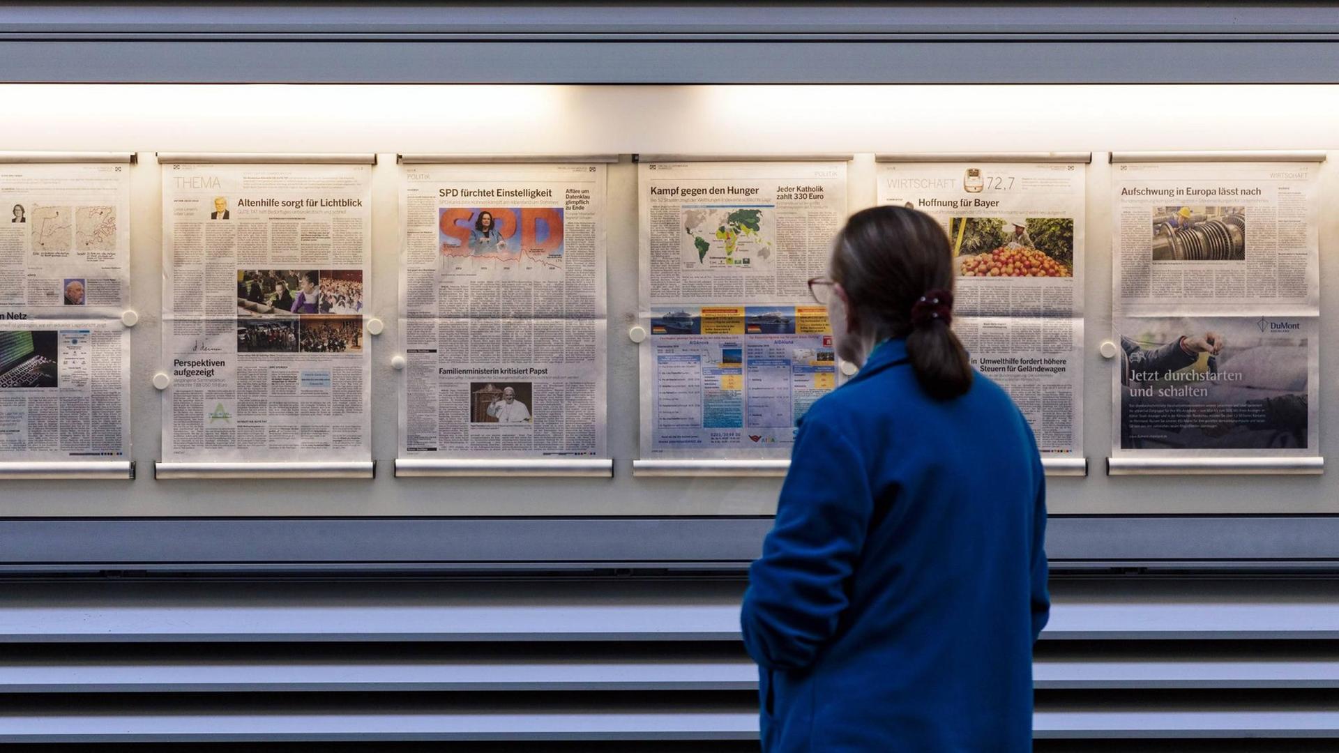 Eine Passantin betrachtet in einem Aushang mehrere Zeitungsseiten.